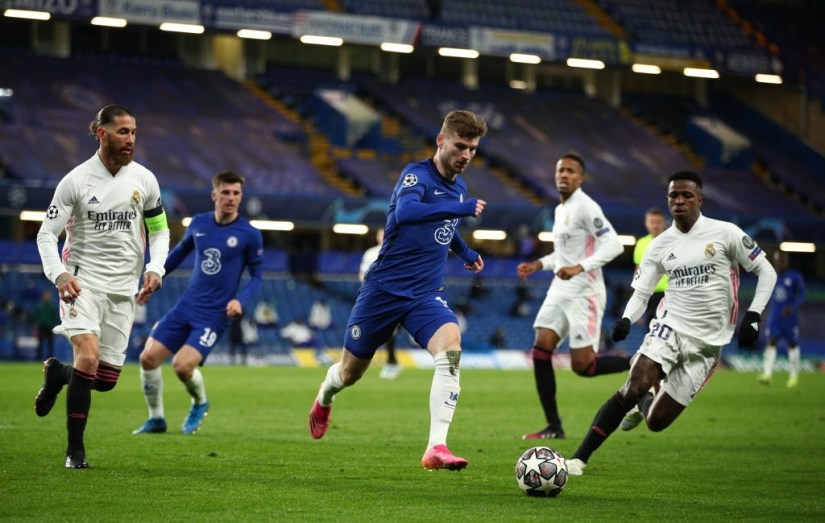 LONDON, ENGLAND - MAY 05: Timo Werner of Chelsea runs with the ball under pressure from Sergio Ramos (L) and Vinicius Junior (R) of Real Madrid  during the UEFA Champions League Semi Final Second Leg match between Chelsea and Real Madrid at Stamford Bridge on May 05, 2021 in London, England. Sporting stadiums around Europe remain under strict restrictions due to the Coronavirus Pandemic as Government social distancing laws prohibit fans inside venues resulting in games being played behind closed doors. (Photo by Chris Lee - Chelsea FC/Chelsea FC via Getty Images )